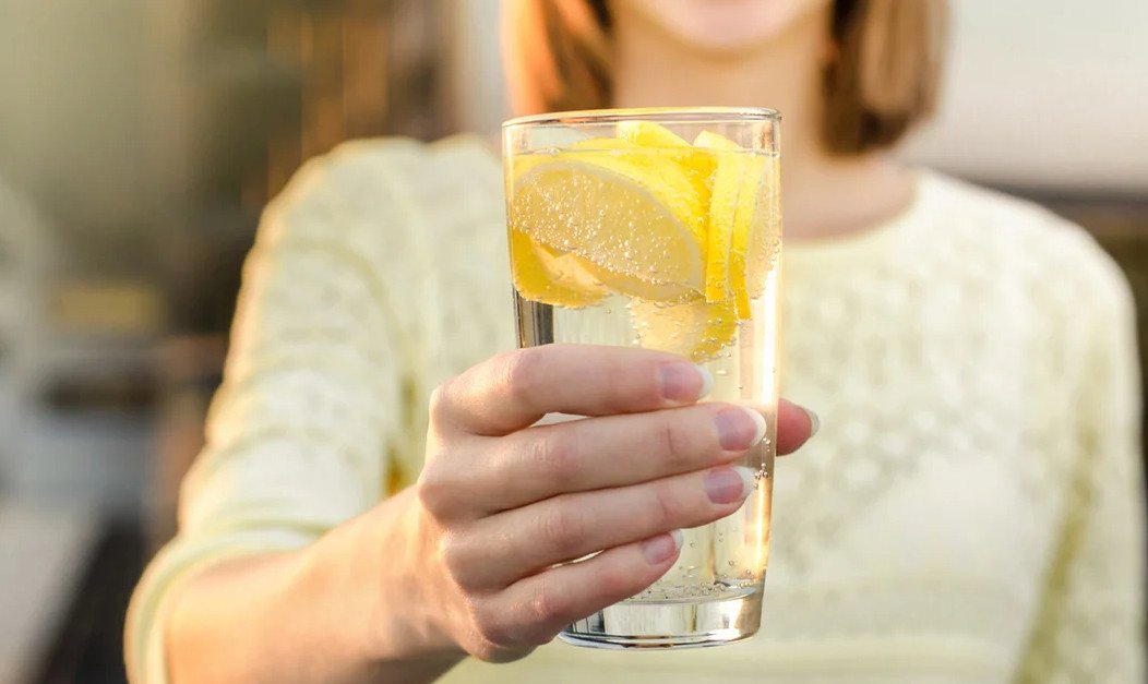 Стакан воды с лимоном. Лимонад в руке. Пить воду с лимоном.
